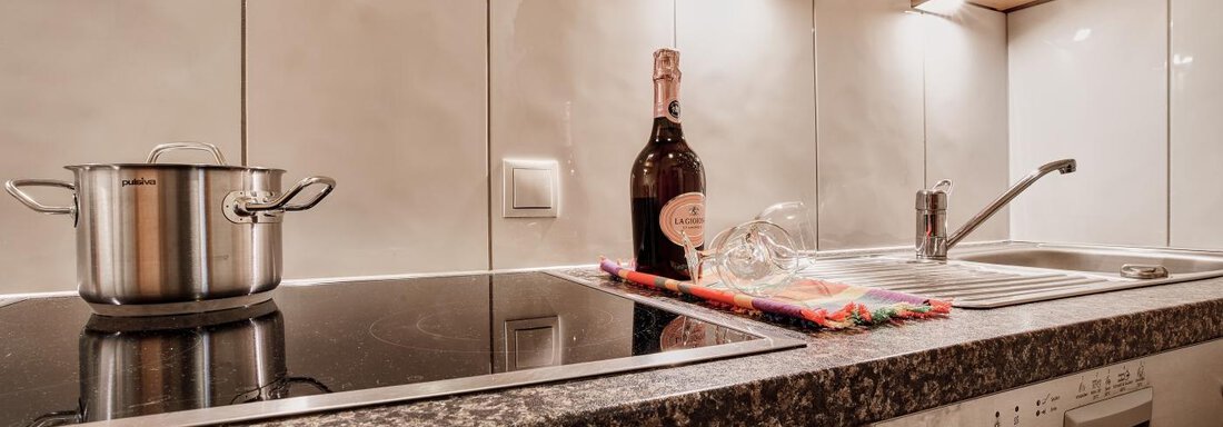 A modern kitchen with a pot on the stove and a bottle of champagne on the countertop. The wooden and stone surfaces give an elegant look. - Belledonne Ski in & out Appartements - Sölden