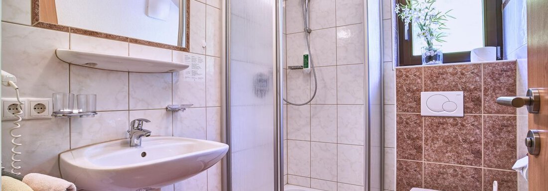 A modern bathroom with a shower, a sink, and a toilet. The walls are brightly tiled, and a window provides daylight. - Belledonne Ski in & out Appartements - Sölden