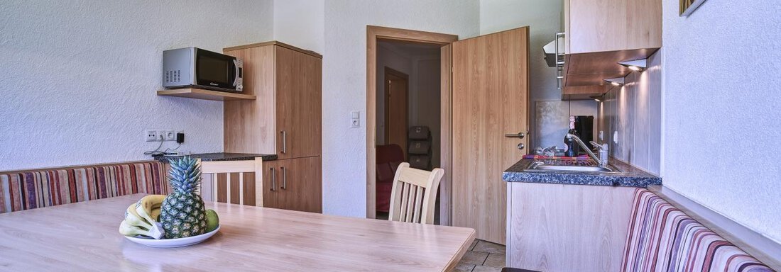 A bright kitchen corner with a round table and a cozy bench. On the table, there is a fruit bowl with bananas and pineapple. - Belledonne Ski in & out Appartements - Sölden