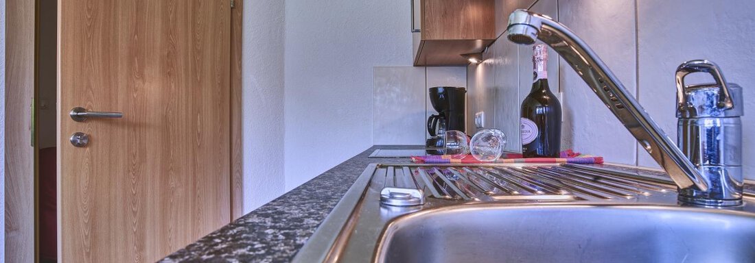 A modern kitchen with a stainless steel sink and a dark granite countertop. In the background, kitchen cabinets and a door can be seen. - Belledonne Ski in & out Appartements - Sölden