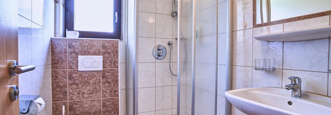 A modern bathroom with a shower, sink, and toilet. Bright tiles and a large window create a pleasant atmosphere. - Belledonne Ski in & out Appartements - Sölden