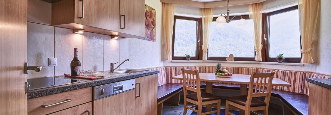 A bright kitchen with wooden cabinets and modern appliances. A dining area with a round table and comfortable benches invites you to linger. - Belledonne Ski in & out Appartements - Sölden