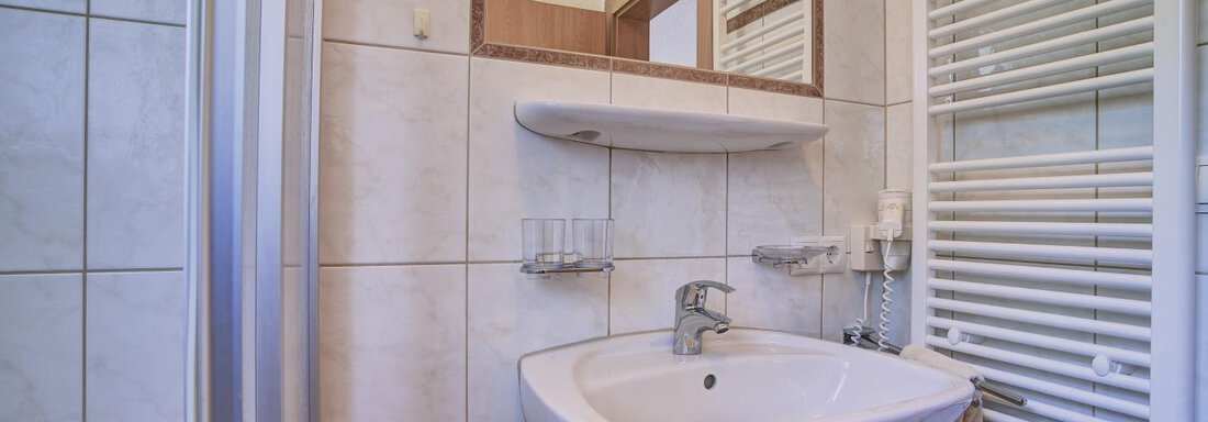 A modern bathroom with a sink and a mirror. The walls are tiled and there is a towel radiator. - Belledonne Ski in & out Appartements - Sölden