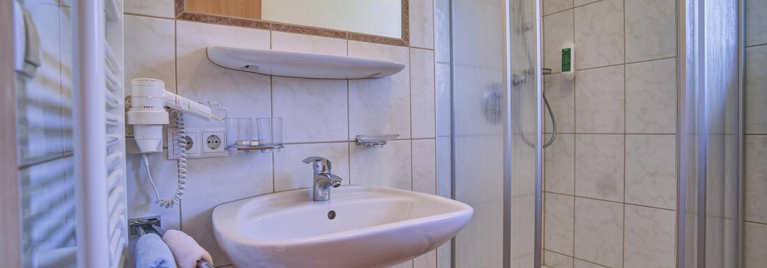 A modern bathroom with a shower and a sink. Towels hang on the wall and a mirror is present. - Belledonne Ski in & out Appartements - Sölden