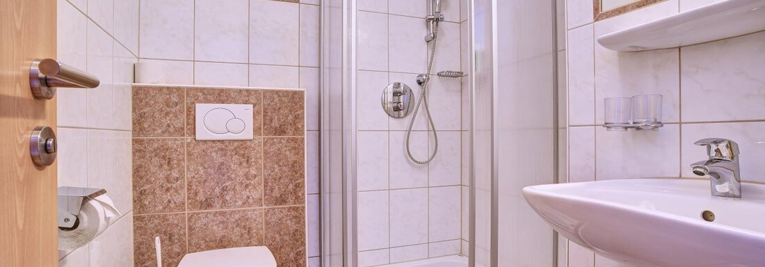 A modern bathroom with a shower, toilet, and sink. The tiles are bright and clean, giving a well-kept impression. - Belledonne Ski in & out Appartements - Sölden