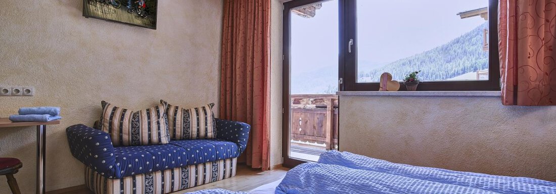 A cozy bedroom with two beds and a blue blanket. Large windows offer a view of the mountains and the room has an inviting atmosphere. - Belledonne Ski in & out Appartements - Sölden