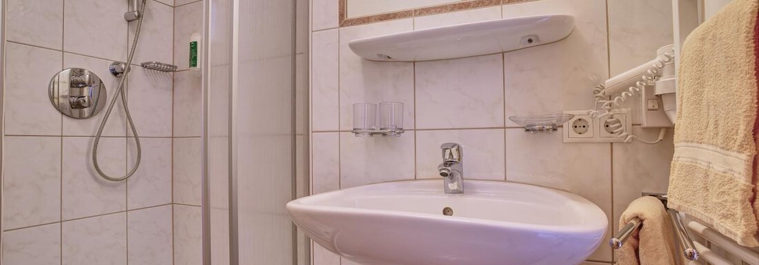 A small bathroom with a shower, a sink, and modern fixtures. The walls are tiled and there are towels as well as a bath mat. - Belledonne Ski in & out Appartements - Sölden