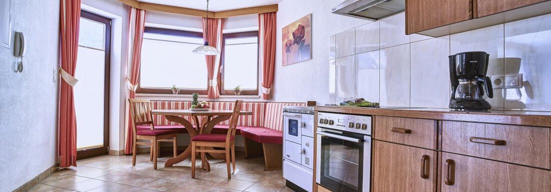 A cozy kitchen with a round table and chairs. The walls are painted in warm colors and light streams through large windows. - Belledonne Ski in & out Appartements - Sölden