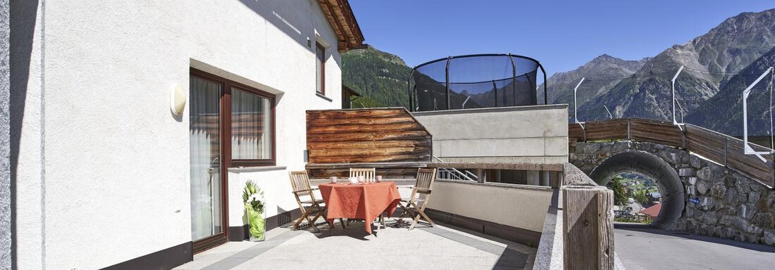 A sunny terrace with a table and chairs. In the background, mountains and a bridge can be seen. - Belledonne Ski in & out Appartements - Sölden
