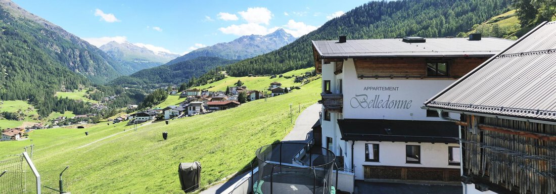 A picturesque mountain landscape with a charming accommodation and green meadows. In the background, tall mountains and a bright blue sky are visible. - Belledonne Ski in & out Appartements - Sölden