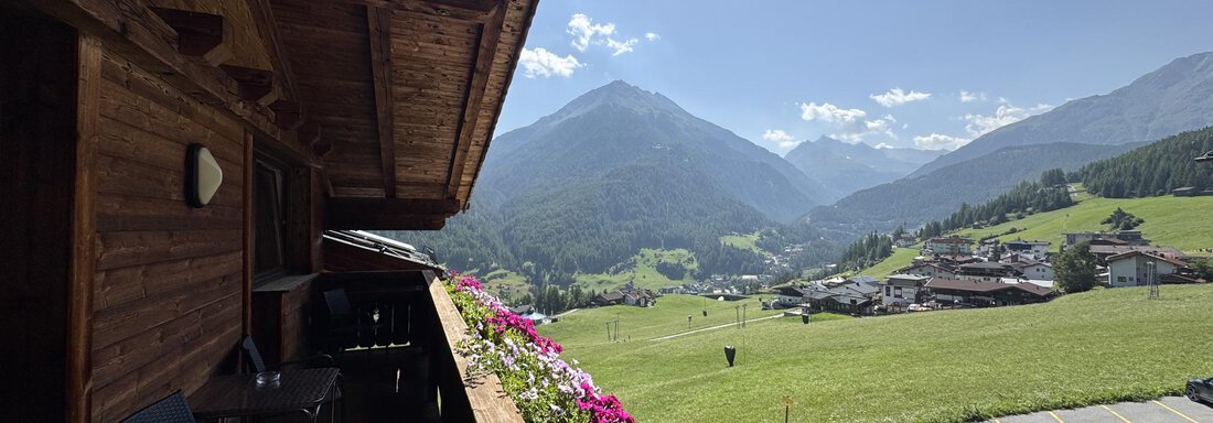 A beautiful view from a balcony of green mountains and a charming village. Colorful flowers frame the view and the sky is clear and blue. - Belledonne Ski in & out Appartements - Sölden
