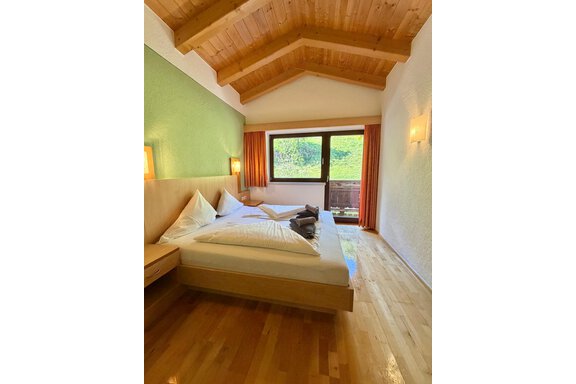 A cozy room with a wooden ceiling and a large window. There are two beds and a pleasant color scheme. - Belledonne Ski in & out Appartements - Sölden
