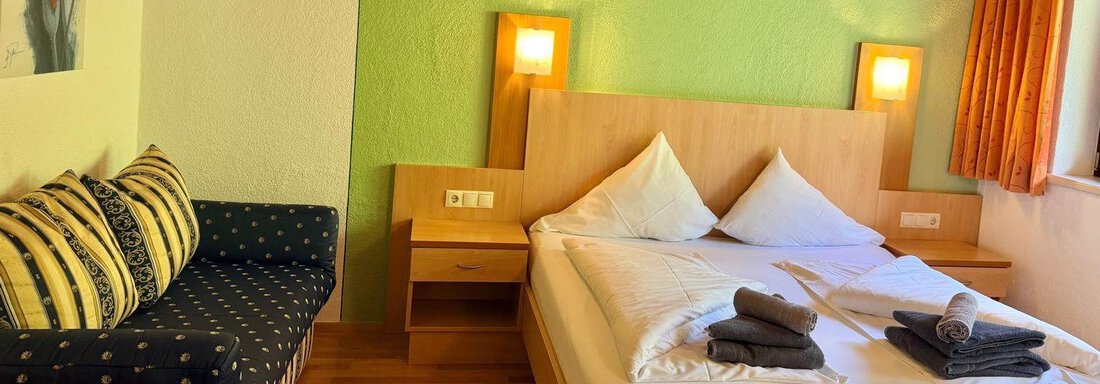 A cozy bedroom with a double bed and a couch. The walls are painted in a soft green tone, and the decoration is simple and modern. - Belledonne Ski in & out Appartements - Sölden