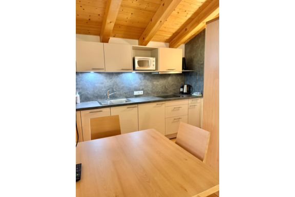 A modern kitchen with a wooden ceiling and light cabinets. On the countertop, there is a microwave and a kettle. - Belledonne Ski in & out Appartements - Sölden