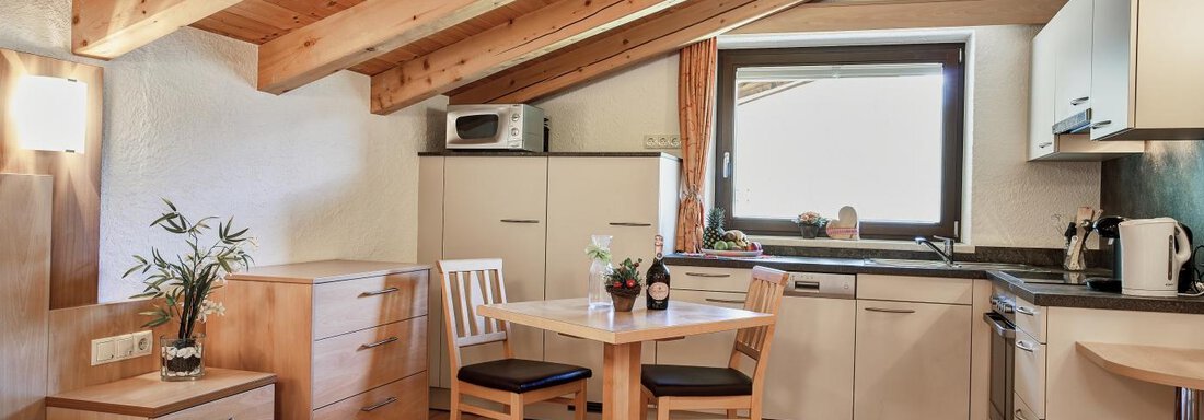 A modern apartment with a cozy living area and a kitchenette. The room features wooden ceilings and large windows offering a view. - Belledonne Ski in & out Appartements - Sölden