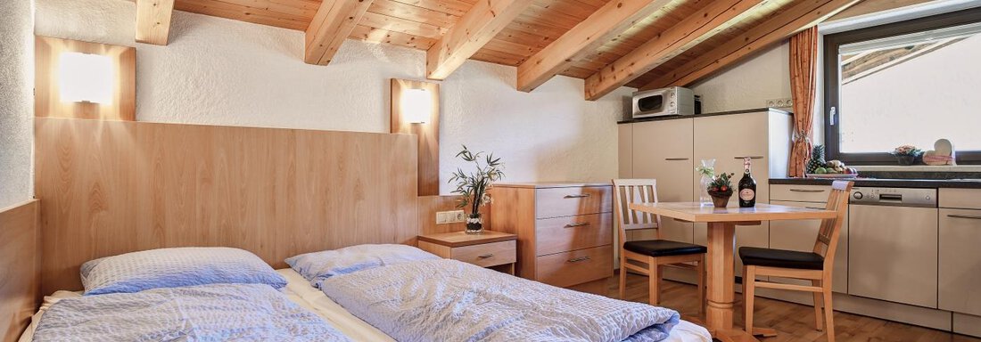 A cozy bedroom with two single beds and wooden paneling. There is a small dining area and a kitchenette. - Belledonne Ski in & out Appartements - Sölden