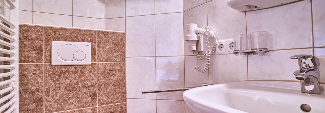A modern bathroom with a shower, sink, and toilet. The walls are tiled and in neutral tones. - Belledonne Ski in & out Appartements - Sölden
