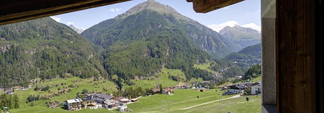 A view of a picturesque mountain landscape with green meadows and a small village in the valley. The majestic mountains extend in the background under a clear sky. - Belledonne Ski in & out Appartements - Sölden