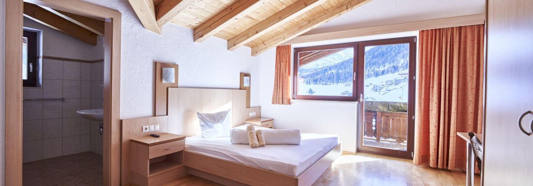 A cozy bedroom with a wooden ceiling and large window. The room is bright and furnished in a modern style. - Belledonne Ski in & out Appartements - Sölden