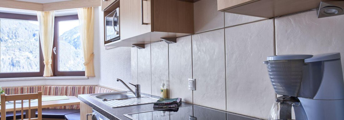 A modern kitchen with bright wood design and windows that let in a lot of daylight. In the foreground, there is a coffee machine and cooking surfaces. - Belledonne Ski in & out Appartements - Sölden