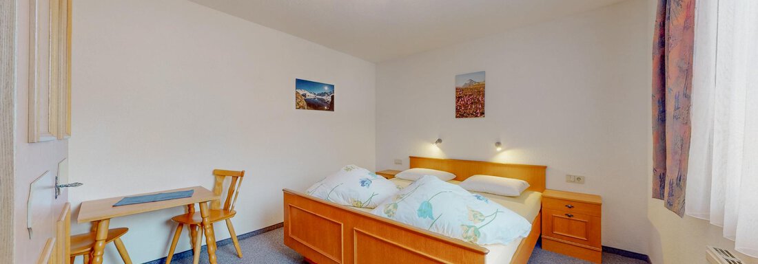 A cozy bedroom with a large bed and two nightstands. There is a small table with chairs and bright walls. - Belmonte Sölden - Sölden
