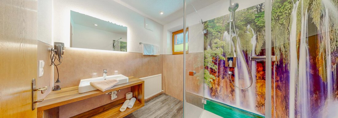 A modern bathroom with a shower and a large mirror. The walls are decorated with a picture of waterfalls and the fittings are elegant and functional. - Belmonte Sölden - Sölden