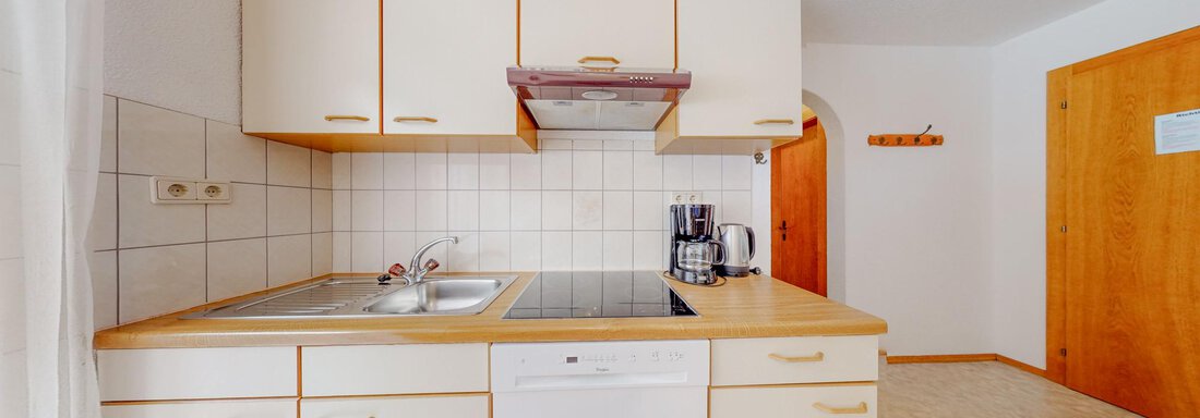 A modern kitchen setup with bright cabinets and a stove. In the corner stands a kettle and the walls are brightly tiled. - Belmonte Sölden - Sölden