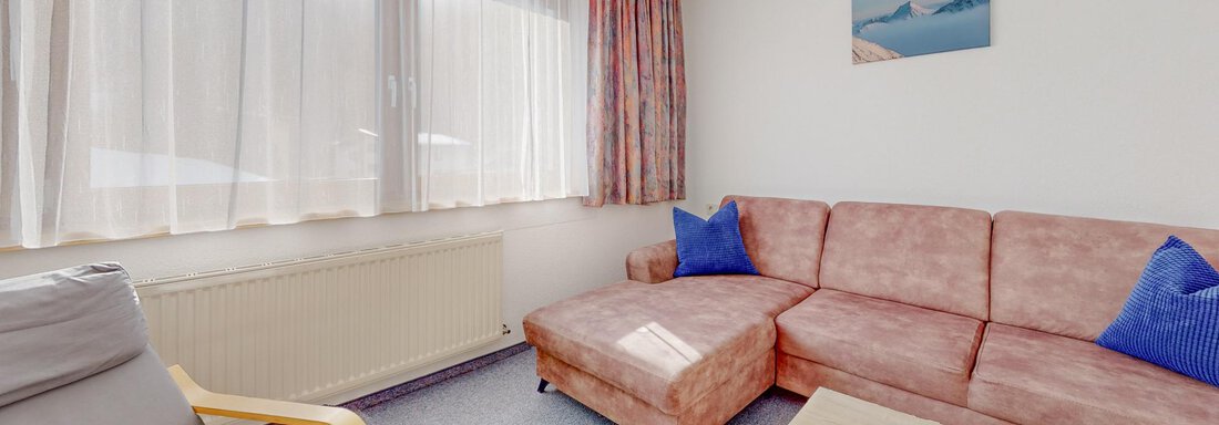 A cozy living room with a beige sofa and blue cushions. Large windows provide plenty of daylight. - Belmonte Sölden - Sölden
