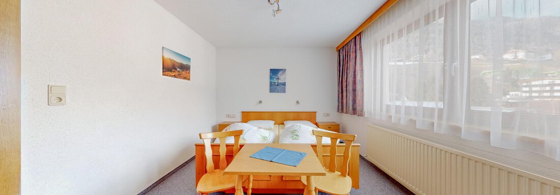 A simple room with a table and chairs. There are two beds and large windows that let in a lot of light. - Belmonte Sölden - Sölden