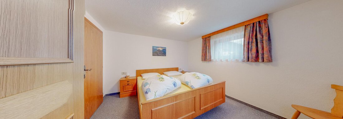 A cozy bedroom with a double bed and colorful bedspreads. The room has natural light and is simply furnished. - Belmonte Sölden - Sölden