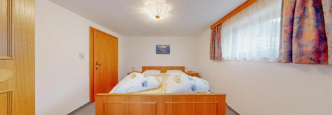 A simple bedroom with a double bed and light-colored walls. Large windows provide plenty of daylight. - Belmonte Sölden - Sölden