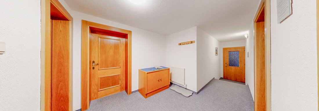 A bright hallway with gray carpet and wooden doors. On the left side, there is a piece of furniture for storage. - Belmonte Sölden - Sölden