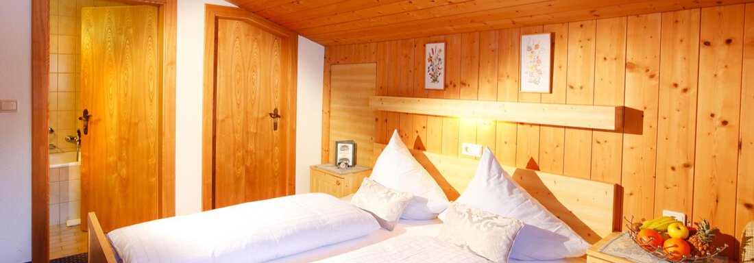A cozy bedroom with wooden walls and two single beds. On the nightstand, there is a fruit bowl, and the doors lead to the bathroom and hallway. - Brandlehof - Sölden