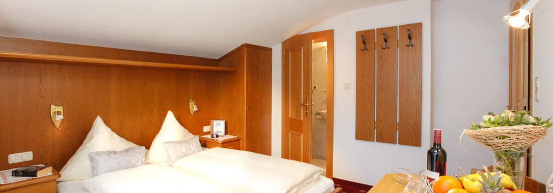 A cozy bedroom with a double bed and wooden-paneled walls. Fresh fruit and a bottle of wine are on the table. - Brandlehof - Sölden