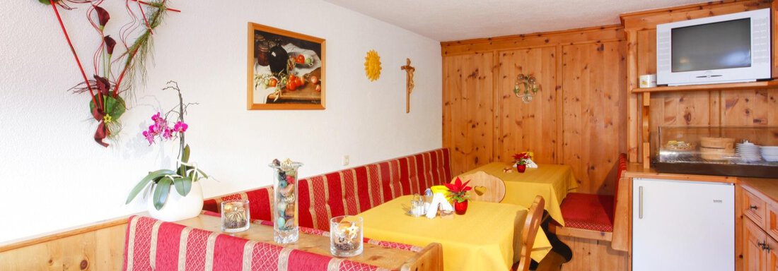 A cozy dining area with wooden paneling and red benches. Flowers and decorative elements adorn the tables, and a television can be seen in the corner. - Brandlehof - Sölden
