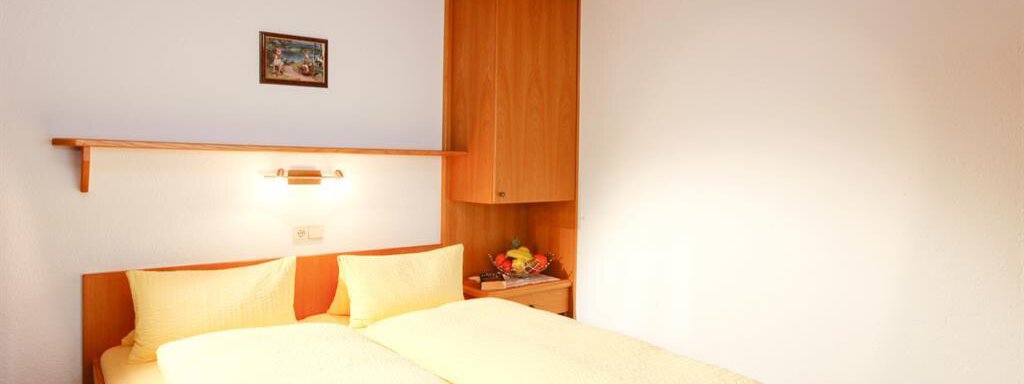 A cozy bedroom with a double bed and soft yellow bedspreads. A small picture hangs on the wall, and the wooden walls give the room a warm atmosphere. - Brandlehof - Sölden