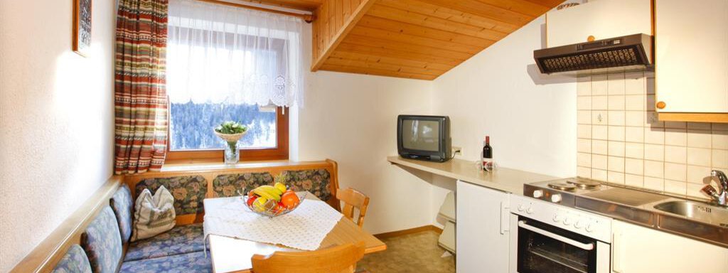 A cozy kitchen with a dining area and a couch. The wooden ceiling and the windows create a warm atmosphere. - Brandlehof - Sölden