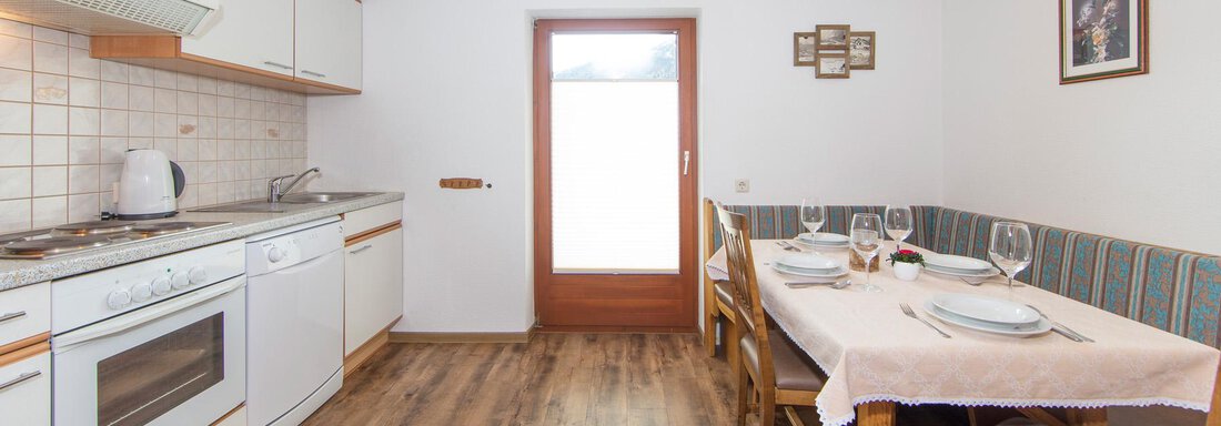 A bright kitchen with a seating area and a table for four people. The walls are plain and the atmosphere is friendly. - Brandlehof - Sölden