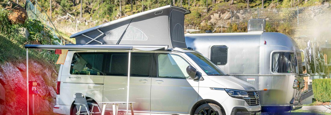 Stellplatz Standard Sommer A modern camper van is parked in a beautiful spot. In the background, you can see a silver travel trailer and a green meadow with trees. - Camping Sölden - Sölden