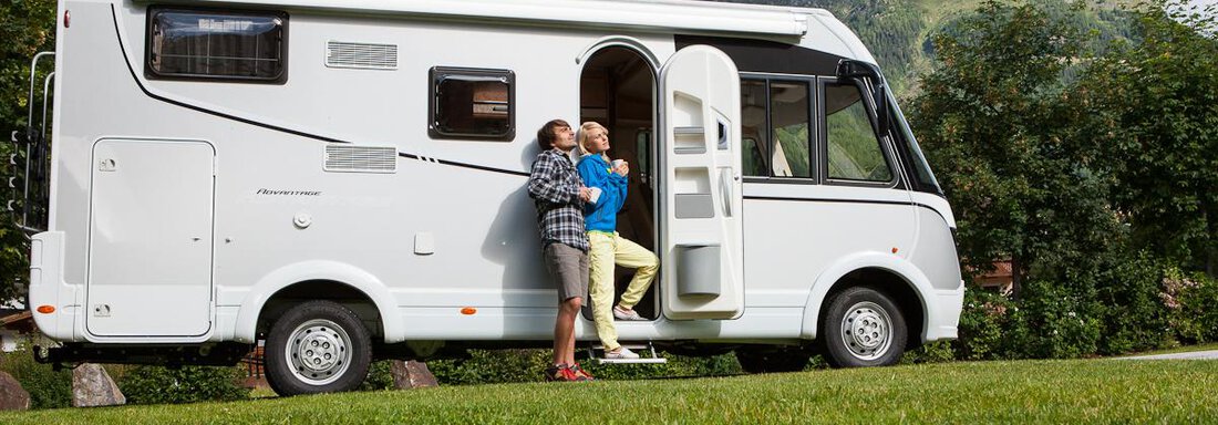 Ein Wohnmobil steht auf einer grünen Wiese mit Bergen im Hintergrund. Zwei Personen stehen davor und genießen die Aussicht. - Camping Sölden - Sölden