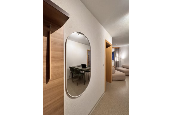 A modern interior with a mirror and a table with chairs. On the other side, there is a cozy seating area and a window. - CASA bianco DUE - Sölden