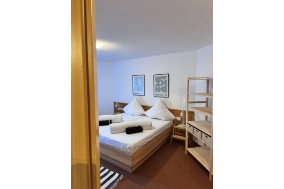 A modern bedroom with two beds and stylish pillows. Decorative pictures hang on the wall, and a shelf stands in the room. - CASA bianco DUE - Sölden