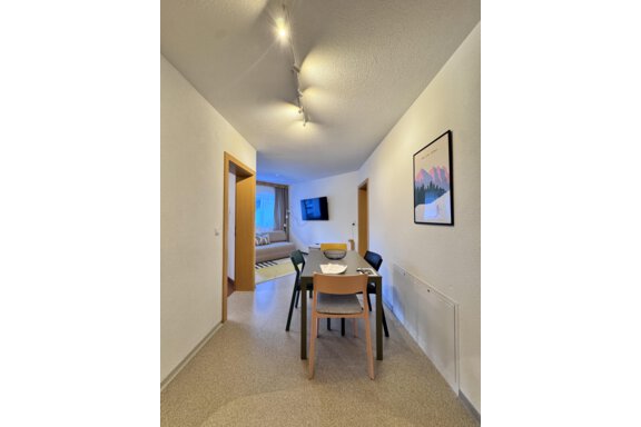 A modern hallway with a table and chairs. In the background, there is a living room with a television and a window visible. - CASA bianco DUE - Sölden