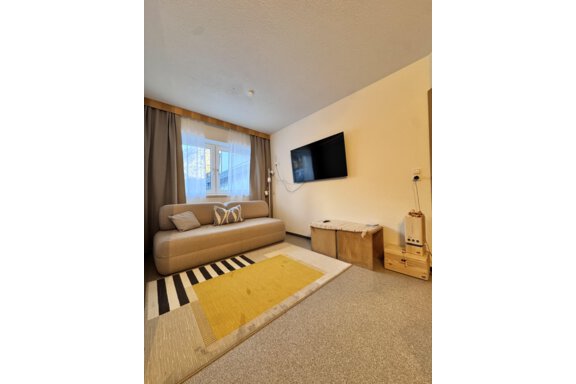 A cozy living space with a beige sofa and a large television on the wall. The floor is decorated with a colorful rug and a yellow runner. - CASA bianco DUE - Sölden