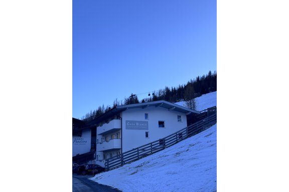 A cozy house in the mountains, surrounded by snow. In the background, there are snow-covered trees and a blue sky. - CASA bianco DUE - Sölden