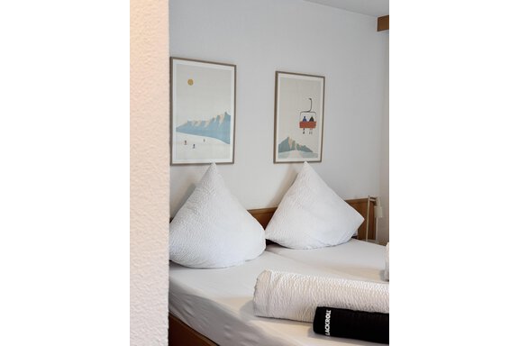 A cozy bedroom with a double bed and large cushions. On the wall, two pictures featuring mountain motifs are hanging. - CASA bianco DUE - Sölden