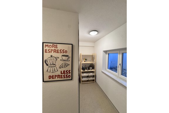 A bright room with a motivational poster that says "More Espresso, Less Depresso." On the right side, there is a shelf with kitchen utensils. - CASA bianco DUE - Sölden