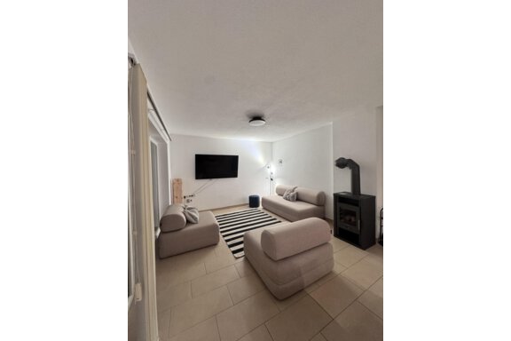 A modern living room with beige sofas and a striped rug. A TV is mounted on the wall and there is a fireplace in the corner. - CASA bianco DUE - Sölden