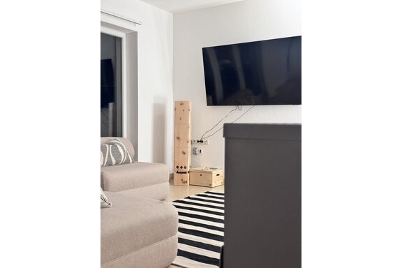 A modern living room with a large TV on the wall. A beige sofa and a striped rug complement the cozy atmosphere. - CASA bianco DUE - Sölden