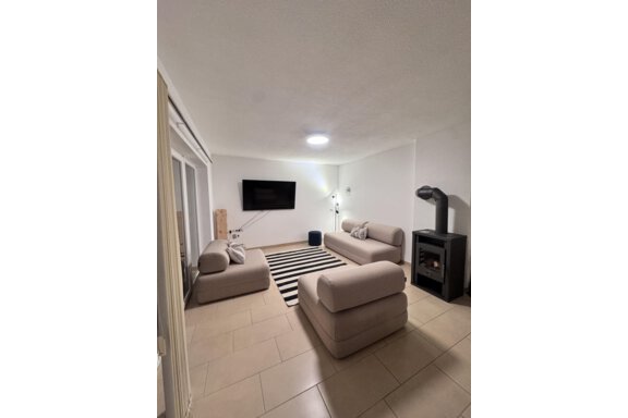 A modern living room with two bright sofas and a black carpet. A TV hangs on the wall, and a fireplace stands in the corner. - CASA bianco DUE - Sölden